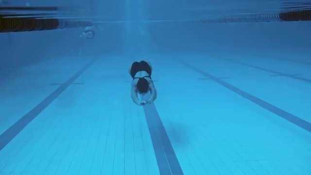 Woman swimming underwater in the pool towards the camera
