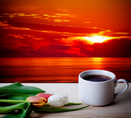 Tea cup with tulips on the wooden table opposite blurred backgro