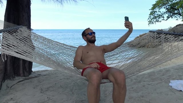 Young man on hammock taking selfie photo with cellphone
