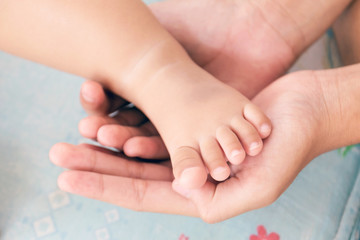 Mother's hand cradles the foot of a baby.