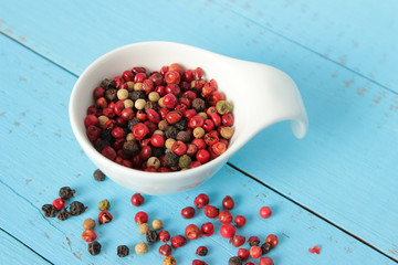 Bunte Pfefferkörner in weißer Schale auf blauem Holzhintergrund
