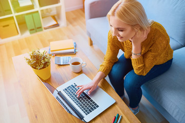 Happy young woman using laptop at home while sitting on sofa
