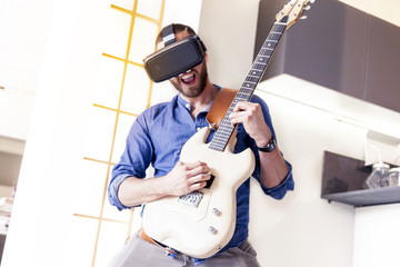 young adult playing guitar at home using viewer for augmented re