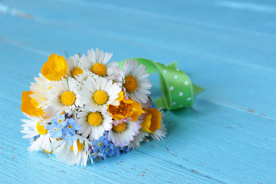 Blumenstrauß mit selbst gepflückten Blumen, Gänseblümchen, Sumpfdotterblume, Vergissmeinnicht  auf blauem Holz
