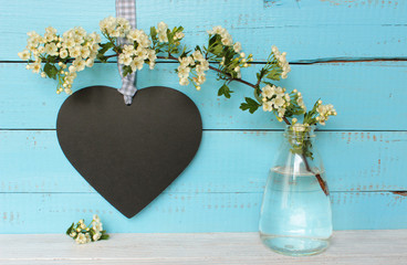 Weißdornzweig in Blumenvase mit schwarzem Herz auf Holz
