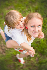 Happy adorable kid boy sitting on his mom's shoulders and laughing. Young blond mother with blond child. Summer vacations. Outdoor. Top view. Happy family.
