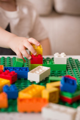 Naklejka premium Close up of child's hands playing with colorful plastic bricks at the table. Toddler having fun and building out of bright constructor bricks. Early learning. stripe background. Developing toys