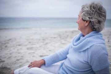 Fototapeta premium Thoughtful senior woman sitting on beach