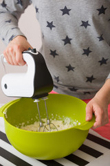 Young woman in long sleeve shirt with stars mixing and tasting dough for homemade muffins. Cooking and baking at home. Bright kitchenware and white mixer. Indoors.