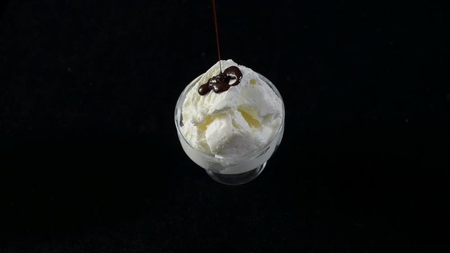 Ice cream in glass Cup pour on top of chocolate syrup on a black background. Full HD, 16:9.