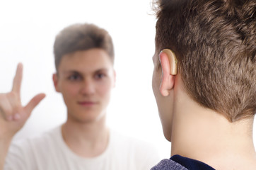 Two deaf-mute teenagers communicating using sign language, selective focus on hearing aid