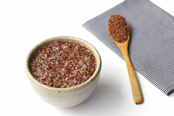 gruel (brown rice) in ceramic bowl and wooden spoon on napery isolated on white background