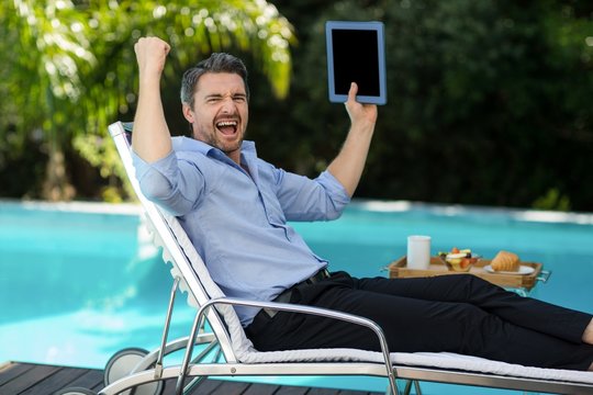 Excited man holding a digital tablet near pool