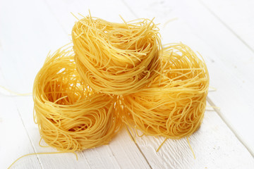 Raw tagliatelle on white wooden background