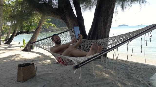 Young man on hammock taking selfie photo with tablet computer
