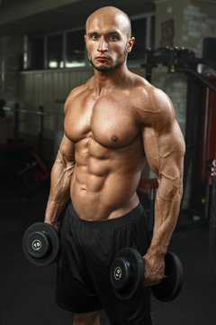 very power athletic guy standing in gym with dumbbells and lokking at camera