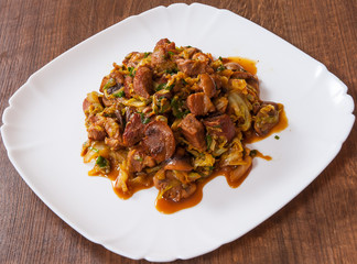 Stewed cabbage with mushrooms and meat in a plate on wooden table