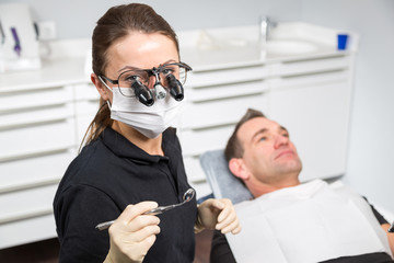 Portrait of dentist with magnifying loupes and patient in the ch