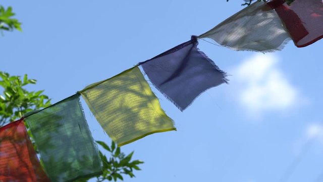 The color Tibetan prayful flags of Lungt (horse of wind) with inscriptions in Tibetan language flutter on wind on background of the blue sky. 4K (UHD)