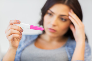 close up of sad woman with home pregnancy test