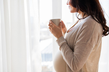 close up of pregnant woman with tea cup at window