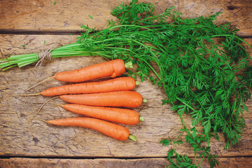 Bunch of fresh carrots with green leaves over wooden background