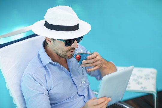 Smart man having martini while using digital tablet near pool - Powered by Adobe