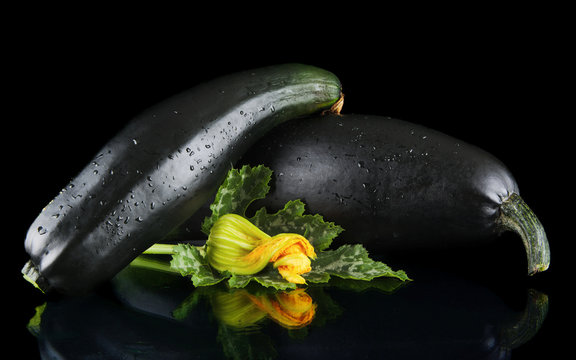 Wet mature courgettes with flowers on black background