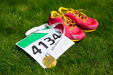 Running shoes,  marathon race bib (number) and finisher medal on grass background, sport, fitness and healthy lifestyle concept
