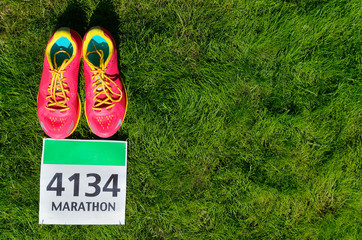 Running shoes and marathon race bib (number) on grass background, sport, fitness and healthy lifestyle concept
