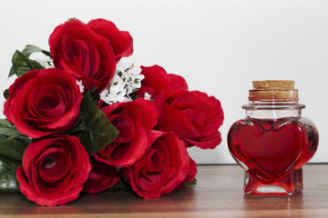 Heart shaped bottle next to a bouquet of roses