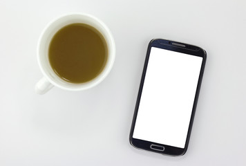Smart phone with blank screen sitting next to a cup of coffee isolated on white
