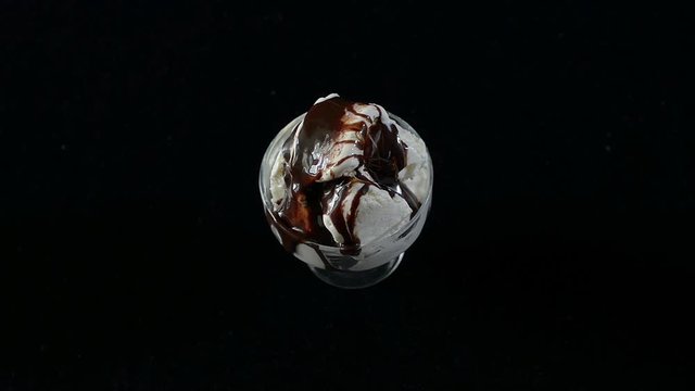 Ice cream with chocolate syrup in glass Cup on the table rotates on a black background. Full HD, 16:9