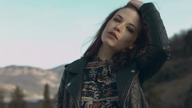 Lovely girl in a dress and leather jacket walking on the parapet 