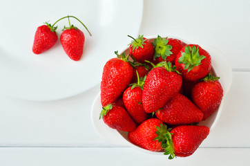 Ripe red strawberries in a white bowl on a white wooden table