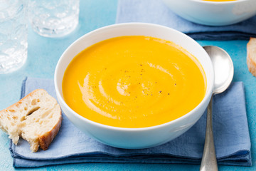 Pumpkin and carrot soup with cream on blue stone background.