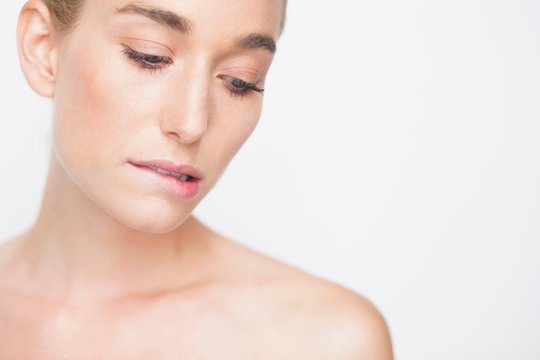 Bare shouldered woman looking down biting lip