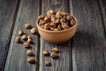 Sugared peanuts in a brown bowl on a wood background