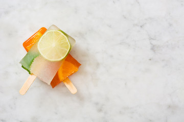 Orange popsicle and lime popsicle on marble table
