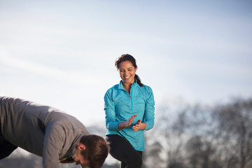 Young woman clapping man doing push up training in park
