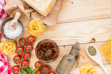 cherry tomatoes fruits, dried tomatoes in glass jar on wooden table, herbs, basil leaf,  thyme, rosemary, prosciutto, pasta, fidelini,  spaghetti, olive oil in clay jug, top view, italian food concept