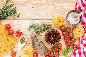 cherry tomatoes fruits, dried tomatoes in glass jar on wooden table, herbs, basil leaf,  thyme, rosemary, prosciutto, pasta, fidelini,  spaghetti, olive oil in clay jug, top view, italian food concept