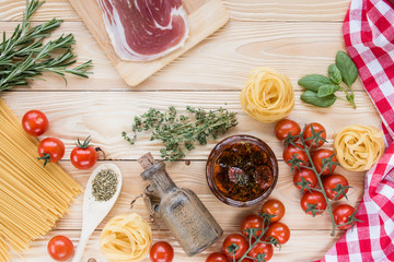 cherry tomatoes fruits, dried tomatoes in glass jar on wooden table, herbs, basil leaf,  thyme, rosemary, prosciutto, pasta, fidelini,  spaghetti, olive oil in clay jug, top view, italian food concept