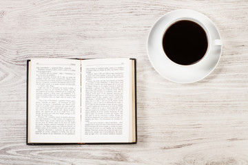 Libro abierto con una taza de café sobre una mesa de madera blanca rústica. Vista superior. Copy space