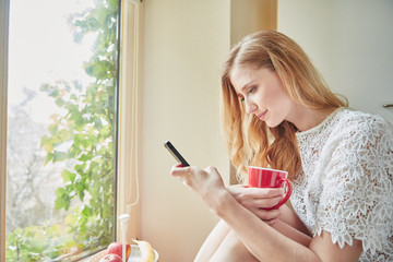 Young woman reading smartphone text in kitchen