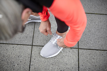 Over shoulder view of mature woman training in city, tying trainer laces