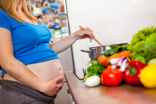 pregnant woman cooking vegetables in kitchen