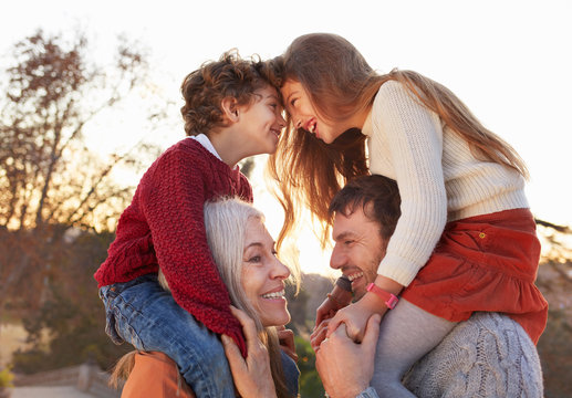 Girl and bot sitting on grandmother and fathers shoulders, head to head smiling