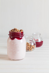Homemade yogurt with jam and walnuts in a jar on a white wooden