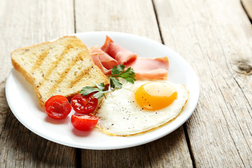 Fried eggs with bacon and toasts on plate on grey wooden table